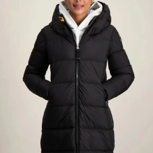 Svart lång dunjacka Parajumpers - Säljer en svart lång dunjacka från Parajumpers med huva och dragkedja framtill. Jackan har quiltad design, två fickor med dragkedja och klassisk logga på ärmen. Perfekt för kalla dagar och riktigt snygg passform.