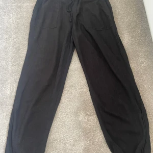 Svarta linnebyxor med snörning - Svarta linnebyxor med avslappnad passform och breda ben. Byxorna har resår i midjan och längst ner på byxorna. Stora fickor både fram och bak. Använd fåtal gånger.