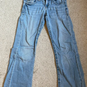Ljusblå bootcut jeans från Gina Tricot - Ljusblå jeans från Gina Tricot med bootcut passform och råa, fransiga benslut. Klassisk femficksmodell, dubbla knappar i midjan och snygga slitningar framtill. Perfekta för en avslappnad och trendig look. Jag har sprättat upp dem där nere så att de ska bli längre. Men överlag ett par jättefina jeans!!! Pris kan diskuterassss💗💗
