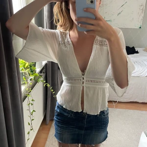 Vit blus med vida ärmar och spetsdetaljer - Säljer en superfin vit blus med djup v-ringning, knappar framtill och snygga spetsdetaljer vid axlar och midja.