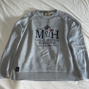 Morris tröja - Snygg grå stickad tröja från Morris med broderad text och brittisk flagga framtill. Tröjan har ribbade muddar vid ärmslut och nederkant samt rund halsringning. Storlek XLL men passar L möjligen M