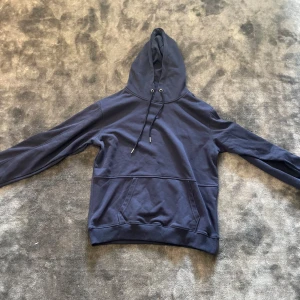 Mörkblå hoodie från C.P. Company - Snygg mörkblå hoodie från C.P. Company med klassisk huva och snörning. Tröjan har en stor magficka och ribbade muddar vid ärmslut och nederkant. Perfekt för dig som gillar stilrena och bekväma plagg.