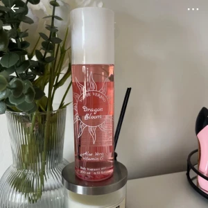 Dragon Bloom body mist - Dragon Bloom body fragrance mist från Sol de Verano med fräsch rosa vätska i en genomskinlig plastflaska. Innehåller aloe vera och vitamin E. Flaskan har vit kork och solmotiv på etiketten. Perfekt för dig som gillar fruktiga och blommiga dofter.
