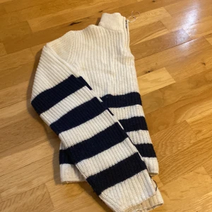 Randig stickad tröja från ONLY - Säljer en ribbstickad tröja från ONLY i vitt och marinblått med breda ränder. Tröjan har hög krage med dragkedja i halsen och långa ärmar. Perfekt för dig som gillar en klassisk och chill stil.