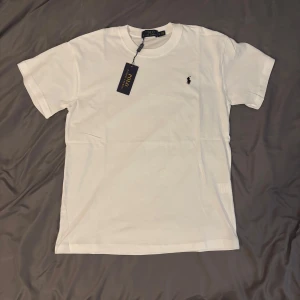 Vit t-shirt Polo Ralph Lauren - Klassisk vit t-shirt från Polo Ralph Lauren med broderad svart logga på bröstet. T-shirten har rund hals, korta ärmar och är 100% mjuk bomull. Skriv om du har några frågor:)