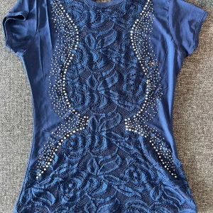 Blå blus med spets och stendetaljer - Supersnygg blå blus med korta ärmar, spets framtill i blommigt mönster och massor av små stenar som ger extra bling. 