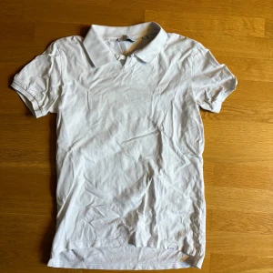 Vit pikétröja från Les Deux - Klassisk vit pikétröja från Les Deux med korta ärmar och snygg krage. Tröjan är i mjuk bomull och har en stilren look. Enkel och fräsch design med diskret logga på bröstet.