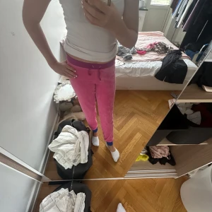 Rosa mjukisbyxor med lila midja - Säljer ett par rosa mjukisbyxor med lila midja och dragsko. Byxorna har smal passform och blå muddar vid bensluten. Perfekta för chill dagar eller när du vill vara extra comfy. Materialet är mjukt och stretchigt, vilket gör dem riktigt sköna att ha på sig.