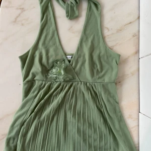 Ljusgrönt linne från Vila - Supersöt ljusgrönt skirt linne från Vila med djup v-ringning. Linnet har plisserad kjol, broderad blomdetalj på bröstet och knyt runt nacken. Perfekt för sommarens alla tillfällen!