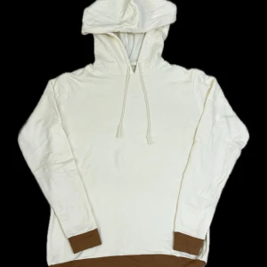 Mjuk vit hoodie med bruna detaljer  - Unik och bekväm hoodie som är handgjord. Färgen är offwhite med brun botten på både ärmarna och nederdelen av tröjan, vilket ger ett stilrent intryck. Passar perfekt att använda hemma eller som en snygg vardagsdetalj. Mjuk insida och skön passform för dig som gillar avslappnade plagg.   Storlek: S/M  Använd men i mycket fint skick! (Kan var felsydd)