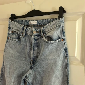Ljusblå raka jeans från Zara - Ljusblå jeans från Zara med hög midja och raka ben. Jeansen har klassisk femficksdesign, råa och fransiga benslut samt en avslappnad vibe. Tillverkade i bomull för en skön känsla och snygg tvättad look.