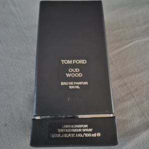 Tom Ford Oud Wood EdP 100ml - Tom Ford Oud Wood Eau de Parfum 100 ml. Lyxig parfym i mörkbrun, fyrkantig glasflaska med svart lock och elegant svart kartong. Doften är känd för sina träiga och kryddiga toner med inslag av oud. Perfekt för dig som gillar exklusiva och unika dofter.