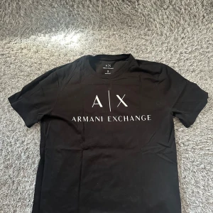 Svart t-shirt från Armani Exchange - Svart t-shirt från Armani Exchange med stort vitt logotryck på bröstet. Klassisk rund halsringning och korta ärmar. Slim fit-modell i mjuk bomull som sitter snyggt och känns skön hela dagen.