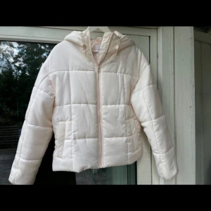 Ljusrosa pufferjacka från Nike - Säljer en ljusrosa/krämfärgad pufferjacka från Nike med huva och dragkedja framtill. Jackan är quiltad med stora rutor och har en clean look. Perfekt för kyliga dagar när du vill vara både varm och snygg. Snygga detaljer med justerbar huva och diskret Nike-logga på bröstet. Aldrig använd. Storleken är Xs men den är mer som en S. Originall priset ca 1000