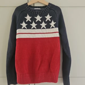 Stickad tröja Tommy Hilfiger stjärnor - Snygg stickad tröja från Tommy Hilfiger i marinblått, rött och vitt. Tröjan har långa ärmar, ribbade muddar och coolt stjärnmönster upptill. Perfekt för dig som gillar klassisk amerikansk stil och vill sticka ut lite extra.