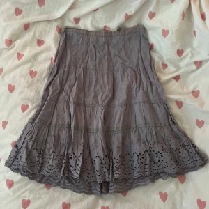 Ljusgrå kjol  - Superfin ljusgrå (lila aktig) kjol i strl S från Noa Noa med broderade detaljer och vågig volangkant nertill. Kjolen har en feminin siluett, dragkedja i sidan och är gjord i mjuk bomull. Perfekt för dig som gillar romantiska och boho-vibbar!💞                                                                           OBS! Defekt nedtill vid kjolen, se sista bilden 