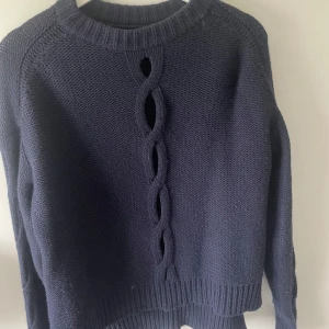 Mörkblå stickad tröja Filippa K - Säljer en mörkblå stickad tröja från Filippa K med snygg flätad detalj och öppningar längs ryggen. Tröjan har ribbade muddar och lång ärm, perfekt för dig som gillar en unik och stilren look.