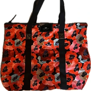 Blommig väska från DAY - Stor och rymlig väska från DAY Birger et Mikkelsen med  blommigt mönster. Väskan har svarta handtag, dragkedja upptill och innerfack med dragkedja. Perfekt för att bära med allt du behöver.