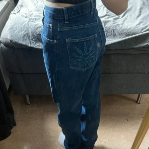 Blå jeans från Viva Jeans Co med brodyr - Säljer ett par blå jeans från Viva Jeans Co med snyggt broderade bakfickor i turkost. Jeansen har högre midja, raka ben och klassisk femficksdesign. 
