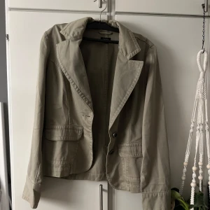 Beige kavaj med fickor från H&M - Stilren beige kavaj från H&M med klassisk krage, två knappar framtill och fickor med lock. Perfekt för en clean och chill look, lätt att matcha med både jeans och kjol. Materialet är mjukt och känns skönt mot huden.