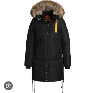 Svart dunjacka Parajumpers pälsluva - Svart lång dunjacka från Parajumpers med stor huva kantad av äkta päls. Finns ett hål i pälsen i luvan, lätt att fixa, då den är använd och finns skavanker så säljer jag den för 3000