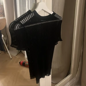 Svart ribbad topp från Zara - Säljer en svart ribbad topp från Zara med korta ärmar. Toppen har en genomskinlig, plisserad look med smala vertikala ränder och en tight passform. Perfekt för dig som gillar en edgy och modern stil.