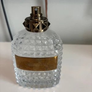 Valentino parfym med nitar (tom flaska) - Snygg parfymflaska från Valentino i transparent glas med rutmönster och guldfärgad metallplatta framtill. Korken har coola nitar och gulddetaljer som ger en lyxig känsla. Perfekt för dig som gillar exklusiva dofter och stilren design.