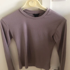 Ljuslila ribbad långärmad tröja Lindex - Säljer en beige ribbad långärmad tröja från Lindex. Tröjan har en enkel rund halsringning och är tillverkad i ett mjukt, stretchigt material som sitter snyggt på kroppen. Perfekt att matcha med jeans eller kjol för en chill look.