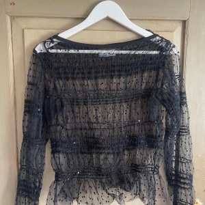 Svart prickig meshblus Holly & Whyte - Säljer en transparent svart meshblus från Holly & Whyte by Lindex. Blusen har långa ärmar, prickigt mönster och volangdetaljer. Perfekt för dig som gillar statement-plagg med coola detaljer och en luftig känsla. Är en M men passar även en S