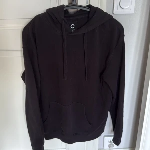 Svart hoodie från Cubus - En klassisk svart hoodie från Cubus med huva samt en stor känguruficka framtill. Tröjan har lång ärm och är tillverkad i mjuk bomull, perfekt för chill dagar eller när du vill ha en enkel och stilren look.