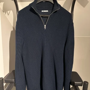 Mörkblå stickad half zip-tröja Zara - Säljer en mörkblå stickad tröja från Zara med half zip-dragkedja och hög krage. Tröjan har lång ärm och är ribbstickad för en snygg struktur. Perfekt för lager-på-lager och chill stil.