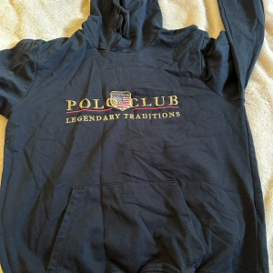 Mörk blå hoodie från Vinson Polo Club - Mörkblå hoodie från Vinson Polo Club med broderad logga och text på bröstet. Skön och avslappnad passform, perfekt för chill dagar eller när du vill ha en sportig look.