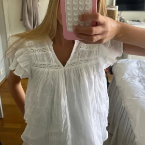 Vit blus med volang från Gina Tricot - Supersöt vit blus från Gina Tricot med volangärmar och v-ringning. Blusen har fina spetsdetaljer och är gjord i ett lätt, luftigt bomullstyg. Från barnavdelningen i storlek 146/152 men skulle säga att den är ungefär som en xxs! 