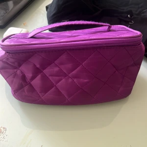 Quiltad lila necessär med dragkedja - Säljer en quiltad lila necessär med praktiskt handtag och dragkedja runt om. Insidan är ljusgul med flera fack för smink eller småprylar. Perfekt att ha med sig i väskan eller på resan. Rymmer mycket och är lätt att hålla ordning i.