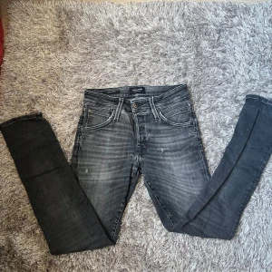 Grå slim fit jeans från Jack & Jones - Snygga grå jeans från Jack & Jones med slim fit och klassisk femficksdesign. Jeansen har en tvättad look med ljusare partier och svarta detaljer vid midjan. Perfekta för dig som gillar en smal siluett och streetinspirerad stil.