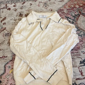 Vit pikétröja från MNG med svarta detaljer - Snygg vit pikétröja från MNG i storlek S. Tröjan har klassisk krage och svarta tunna ränder längs krage och ärmslut. Tillverkad i mjukt stickat material med ribbade muddar. Perfekt för en clean och stilren look.