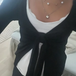 Svart kofta med knyt framtill från ginatricot - Svart kofta med lång ärm och snygg knytning framtill. Perfekt att slänga över ett linne eller topp för en chill och stilren look. Koftan har en klassisk passform och är gjord i ett mjukt material som känns skönt mot huden.