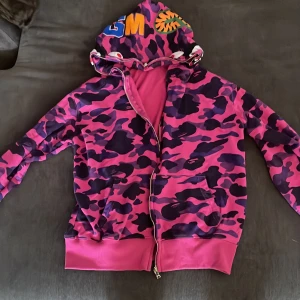 BAPE camo hoodie med dragkedja - Säljer en ikonisk BAPE hoodie i rosa och lila camo med coola broderade detaljer på luvan och hel dragkedja. Dragkedjan är söndrig därav priset men går att fixa!