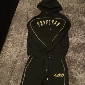 Svarta Trapstar mjukisbyxor med gula detaljer - Svarta mjukisbyxor från Trapstar med gula sömmar längs benen och broderad Trapstar-logga i gult på ena benet. Byxorna har dragsko i midjan och är tillverkade i mjukt bomullsmaterial för en chill och bekväm stil.