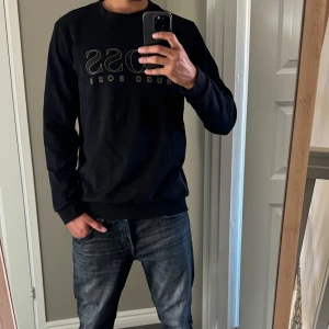 Svart BOSS sweatshirt med logga - Svart sweatshirt från Hugo Boss med stor guldfärgad BOSS-logga på bröstet. Tröjan är väldigt bra skick nästintill oanvänd. Den sitter som M/L, sitter perfekt på mig som är ca 180cm och 75kg. Tveka inte att skriva vid funderingar 💯