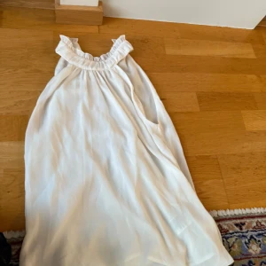 Vit blus med volangkrage - Superfin vit blus med volangdetalj vid halsen och ärmlös design. Klänningen har en luftig och flowy passform, perfekt för varma dagar.