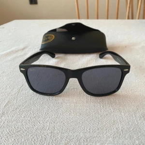 Svarta Ray-Ban Wayfarer solglasögon - Klassiska svarta Ray-Ban Wayfarer RB2140 med mörka glas och ikonisk fyrkantig form. Snygg och tidlös design med Ray-Ban-logga på skalmen. Kommer med original svart fodral. 