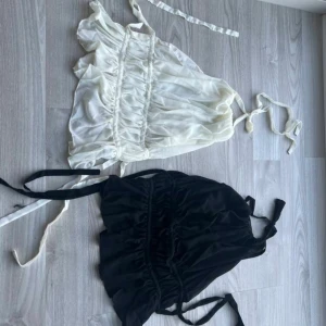 Svart och vit omlott topp från Nelly  - Två superfina omlottlinnen i svart och vitt med tunna axelband och knyt i ryggen, perfekta för sommaren.  Endast använda ett fåtal gånger, i nyskick. Från Nelly – nypris 300 kr/styck. 150 kr/st eller 250 kr för båda! Säljes gärna som set – skriv för snabb deal 💌