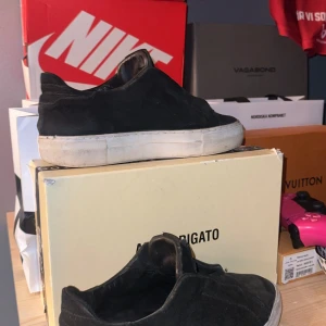 Svarta slip-on sneakers från Axel Arigato - Svarta slip-on sneakers från Axel Arigato i mocka med vit platt sula. Snygg minimalistisk design utan snörning, perfekt för en clean och stilren look. Skorna har rund tå och diskreta detaljer som gör dem lätta att matcha med olika outfits.