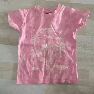Rosa t-shirt med djurtryck från Indiska - Söt rosa t-shirt från Indiska med korta ärmar och vitt tryck av djur, palmer och växter på framsidan. 