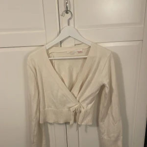Vit omlottkofta med knyt och ribbad kant - Säljer en vit omlottkofta från Gina Tricot med snygg knytning i midjan och bred ribbad kant nedtill. Koftan har långärmade ärmar och är croppad i modellen, perfekt att styla med höga jeans eller kjol. Mjuk och skön bomullskvalitet.