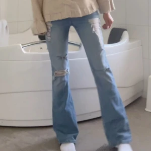 Ljusblå bootcut jeans med slitningar - Snygga ljusblå jeans med bootcut passform och rejält slitna detaljer framtill. Jeansen har låg midja och är tillverkade i klassiskt denimtyg. Perfekta för dig som gillar en trendig och avslappnad look.
