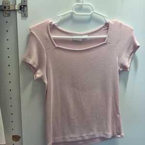 Ljusrosa topp från Gina Tricot - Supersöt ljusrosa topp från Gina Tricot med korta ärmar och unik fyrkantig halsringning. Mjuk och stretchig bomullskänsla, perfekt till jeans eller kjol. Enkel men trendig design som passar till många olika stilar.