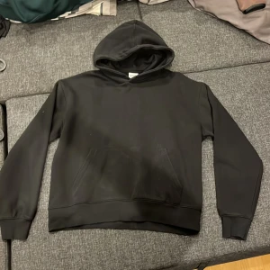 Svart hoodie från Bershka - En stilren svart hoodie från Bershka med klassisk huva och känguruficka framtill. Tröjan har långa ärmar och ribbade muddar. Perfekt för dig som gillar en enkel och clean look. Materialet är mjukt och bekvämt, troligen bomullsmix.