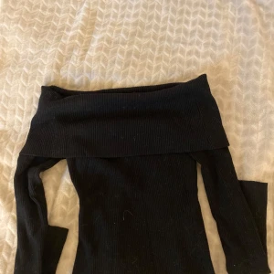 Svart ribbad offshoulder topp H&M - Svart ribbad offshoulder topp från H&M med långa ärmar. Snygg croppad modell som sitter tight och har en bred kant upptill som viker sig över axlarna. Perfekt att styla med jeans eller kjol för en trendig look.